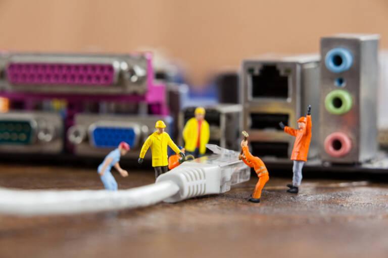 Conceptual image of miniature engineer and worker plug-in lan cable to computer