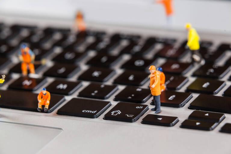 Conceptual image of miniature workmen repairing a laptop keyboard